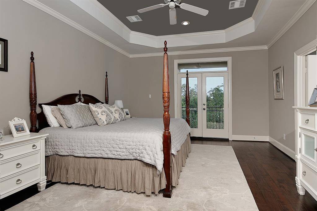 Elegant primary bedroom features an eye-catching tray ceiling, rich hardwood floors and inviting French doors leading to a serene outdoor setting.
