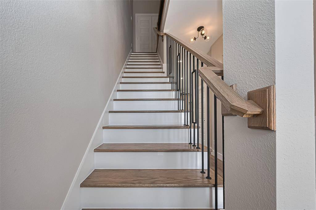 Chic Staircase with Custom DetailsMake a grand transition between floors with this stylish staircase featuring wood-tread steps, clean white risers, and matte black vertical spindles. The natural wood handrail and modern sconce lighting add warmth and architectural interest, elevating the space with timeless design.