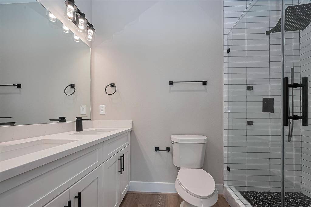 Sleek Modern Bathroom with Walk-In ShowerThis bath is a showstopper—featuring a quartz double vanity with matte black fixtures, a frameless glass walk-in shower, and bold designer tile underfoot. The vertical subway tile adds modern edge, while the spacious layout and updated lighting provide both luxury and function.