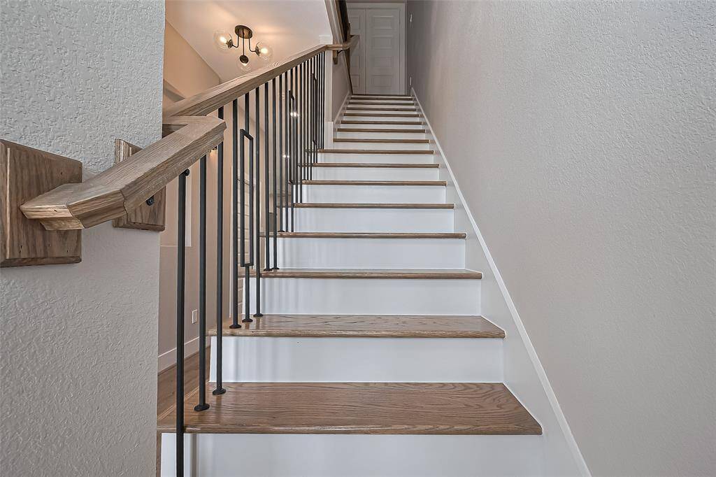 Statement Staircase with Stylish DetailingThis beautifully designed staircase features warm wood treads, crisp white risers, and matte black spindles—leading you from the open-concept main floor to the private upstairs quarters. A modern sconce fixture adds an elegant touch to this transitional space.
