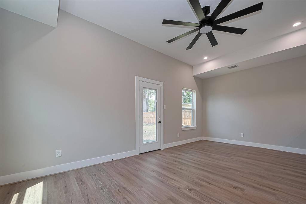 Spacious Living Room with Designer TouchesThis light-filled living space features soaring ceilings, sleek recessed lighting, and an eye-catching modern ceiling fan that elevates the entire room. Durable luxury vinyl plank flooring offers warmth and style, while the back door and windows invite in natural light and provide easy access to the private backyard—perfect for relaxing or entertaining.