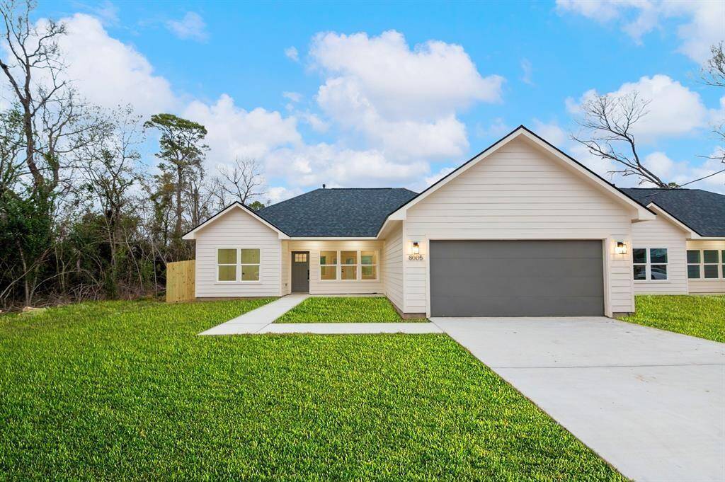 Modern single-story home with a spacious two-car garage, fresh siding, and a neatly manicured lawn. It features a welcoming entryway and large windows, set against a backdrop of mature trees.