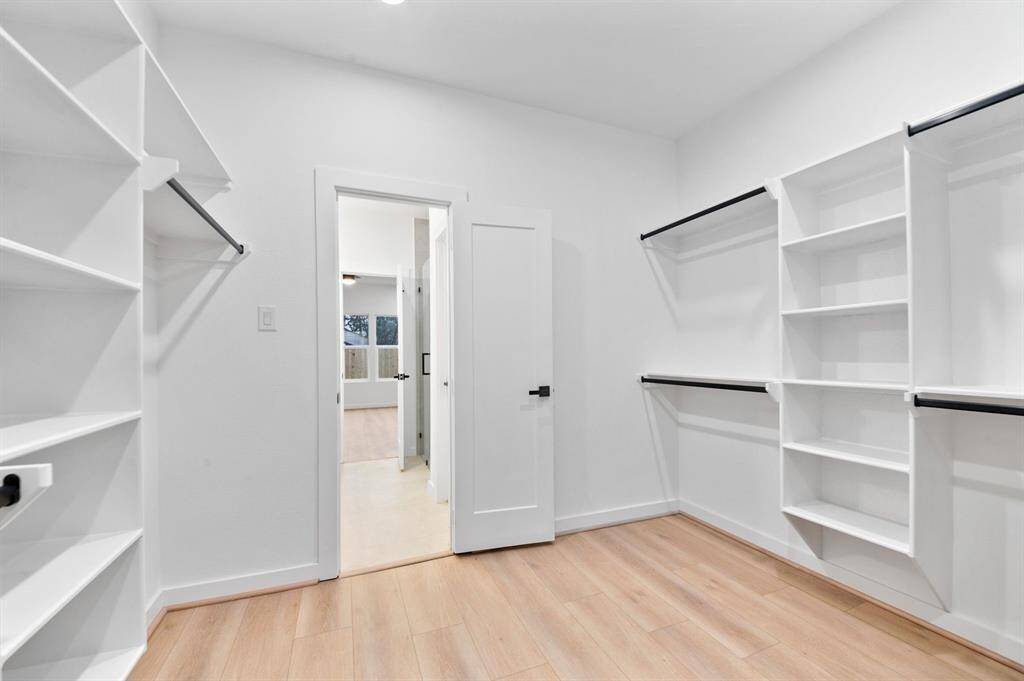 This photo showcases a spacious walk-in closet with ample shelving and hanging space. It features light wood flooring, white walls, and a door leading to another room, offering a bright and organized storage solution.
