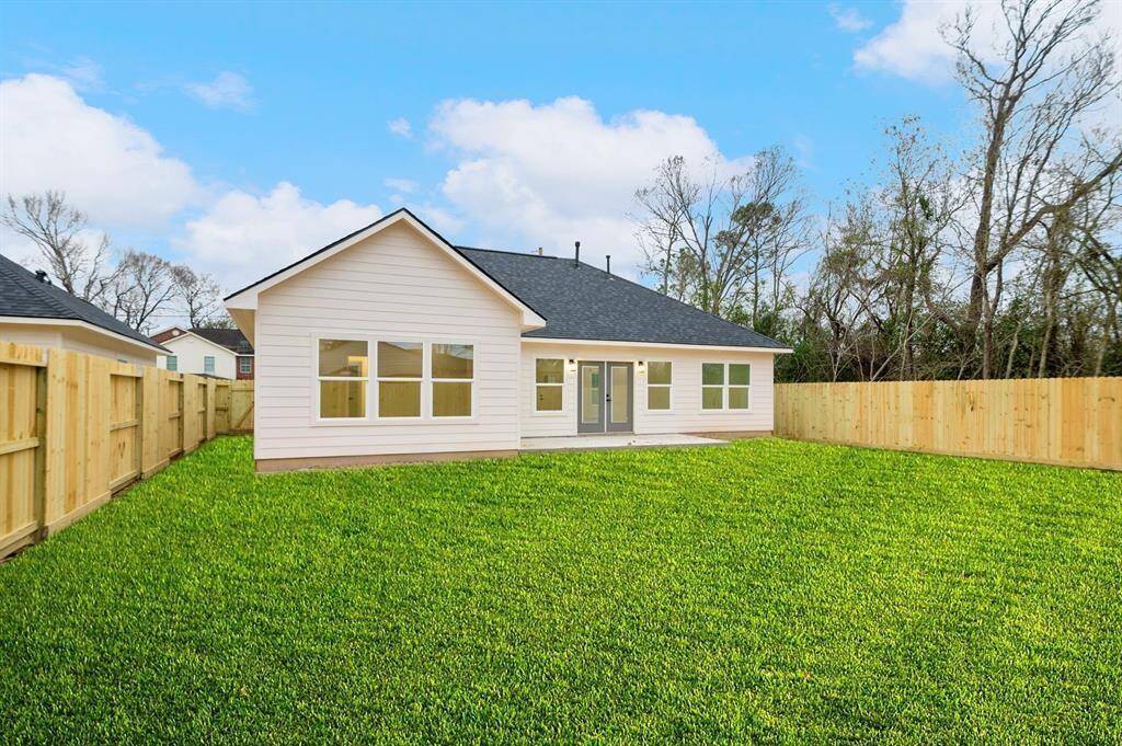 This photo showcases a modern, single-story home with a spacious, well-maintained backyard. The house features a light exterior, large windows, and a fenced-in yard, providing privacy and ample space for outdoor activities.