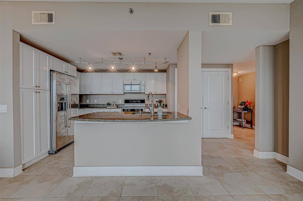 Spacious open-concept kitchen with elegant white cabinets, seamlessly connected to the den.