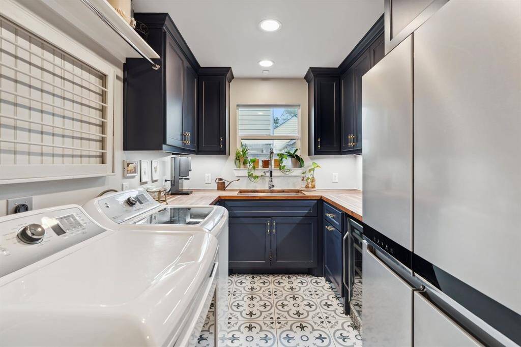 A stylish utility room, complete with a washer and dryer, full-sized fridge, wine cooler, sink, and ample cabinet space.