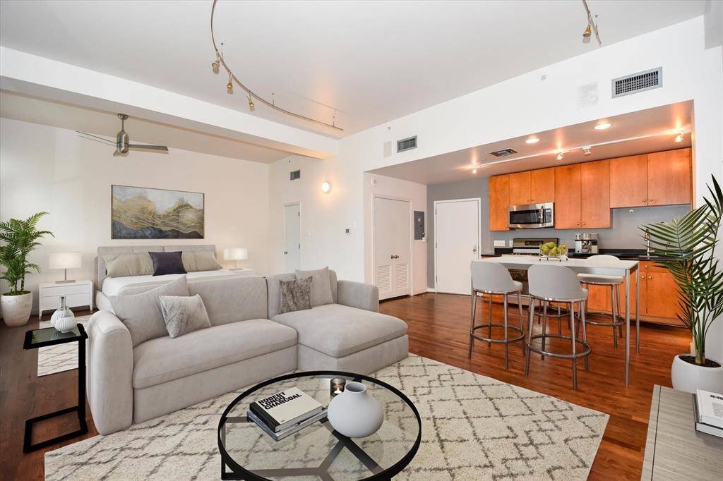 Bright and open loft-style layout featuring a sleek kitchen with dark counters top, spacious living area, and a cozy sleeping space all tied together with stylish lighting and hardwood floors throughout.