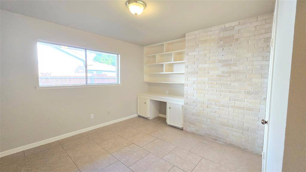 The secondary bedroom features a stunning picture window, filling the room with natural light. The built-in desk and unique brick accent wall add character and functionality, making it a perfect space for work or relaxation.