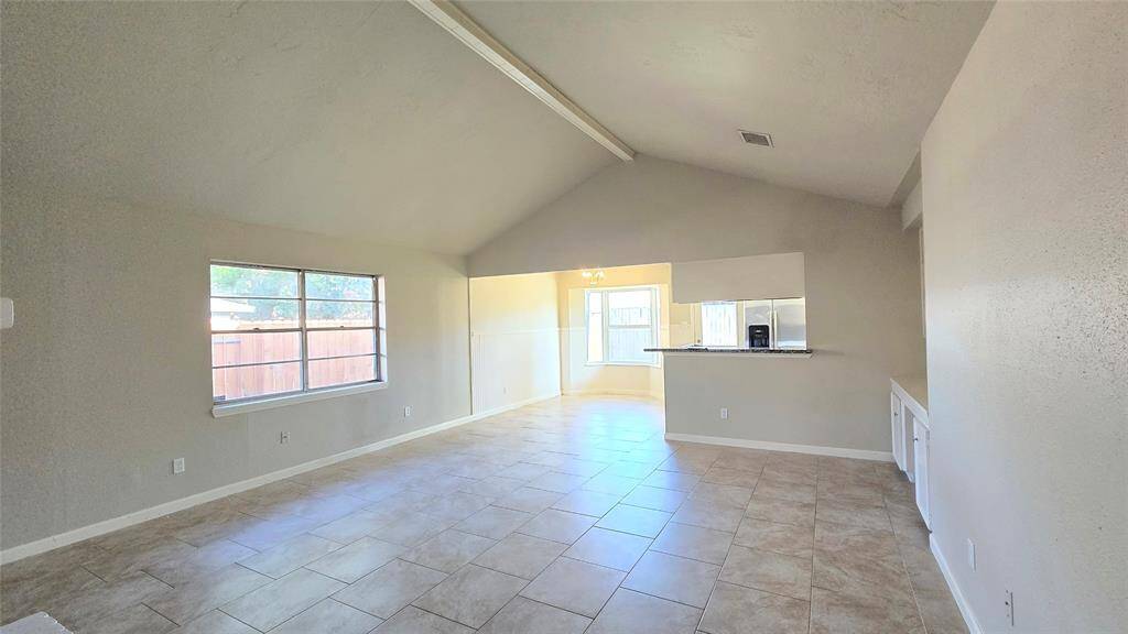 This spacious den area boasts high ceilings and expansive windows that flood the space with natural light. The open floor plan seamlessly connects to the kitchen with a sleek breakfast bar, ideal for entertaining.