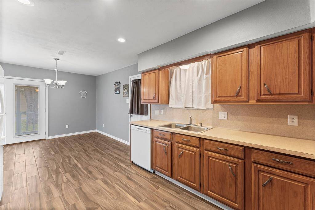 This kitchen features ample wooden cabinetry, a dual-basin sink, and an electric stove. It has a neutral countertop and backsplash, offering a spacious and functional cooking area.
