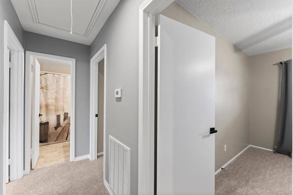 This photo shows a spacious kitchen and dining area with wooden cabinetry, and neutral walls. It features a double sink, dishwasher, and a dining nook with a chandelier. A door leads to an outdoor space, providing ample natural light.