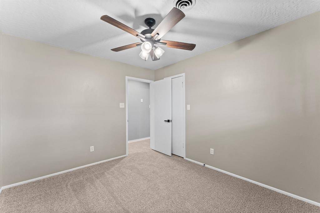 This bedroom features neutral walls and carpet, a ceiling fan with lights, and a window to provide ample natural light.