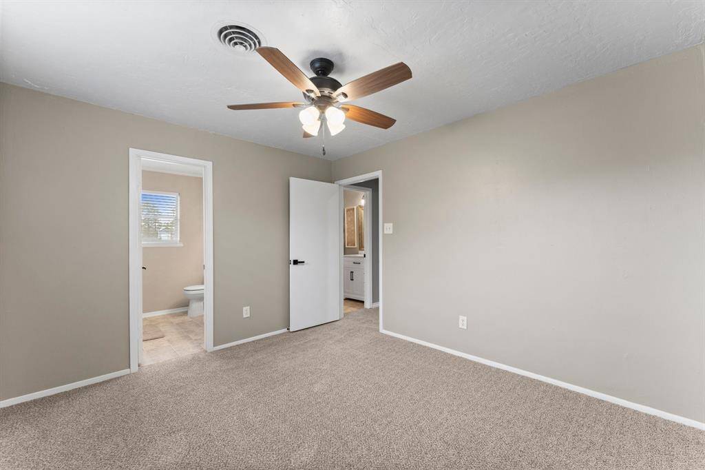 Master bedroom with neutral walls and carpet, featuring a ceiling fan with lights. Window allows for ample natural light.