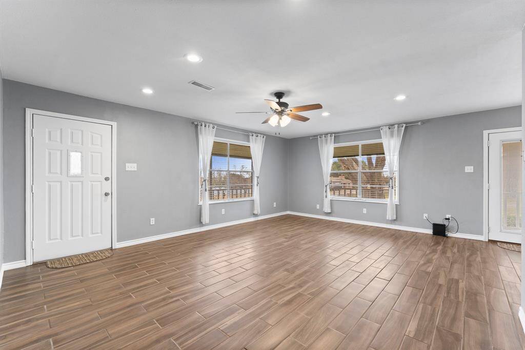 This spacious living area features sleek wood-look tile flooring and ample natural light from large windows. A ceiling fan and recessed lighting add comfort and style, while French doors provide access to the outdoors.