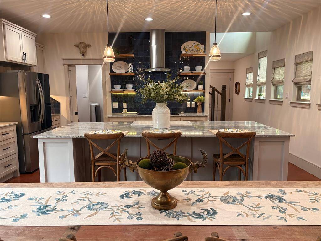 This picture shows the large open kitchen that has custom cabinets, open shelving, undermount lighting, and a huge island.