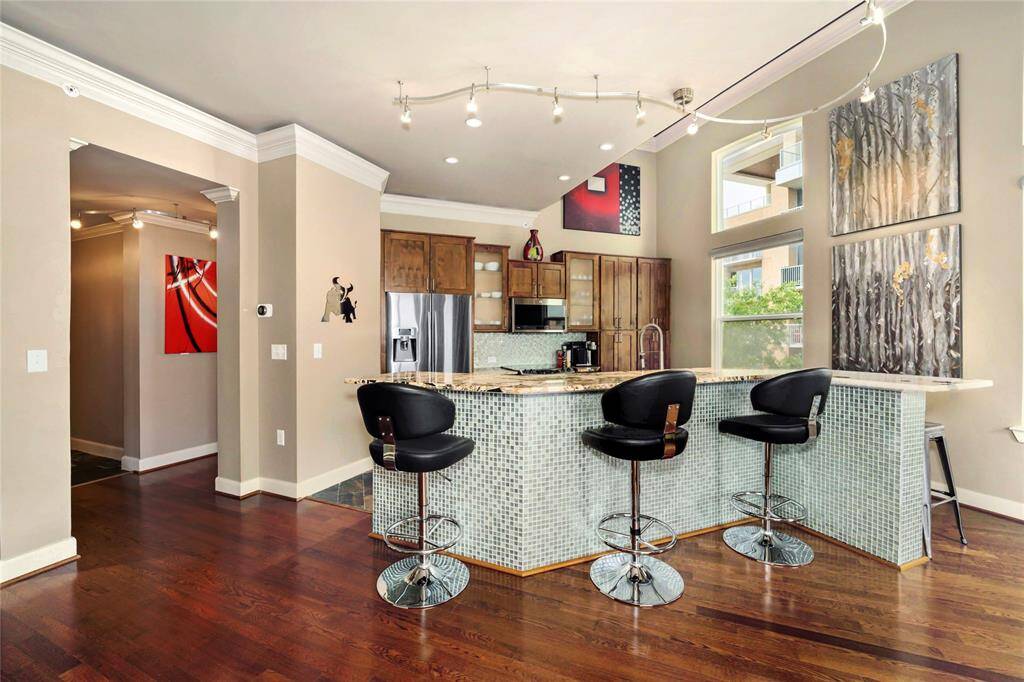 Living room seamlessly opens up to the breakfast bar seating and the kitchen. Long hallway to the left is the entry. The hallway with the red artwork leads to the bar, the hallway full bath and your secondary bedroom. Notice elevated ceilings in this condo where the red/black artwork is.