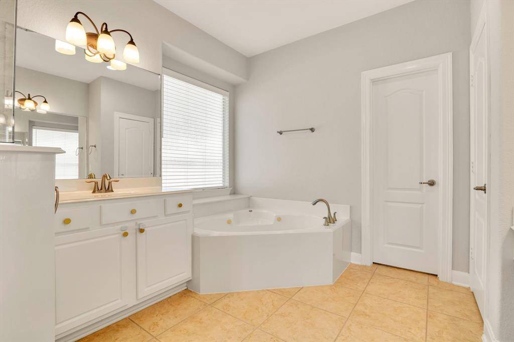 Bright and spacious bathroom featuring a large corner bathtub, dual sinks with ample counter space, elegant lighting fixtures, and a neutral color palette.