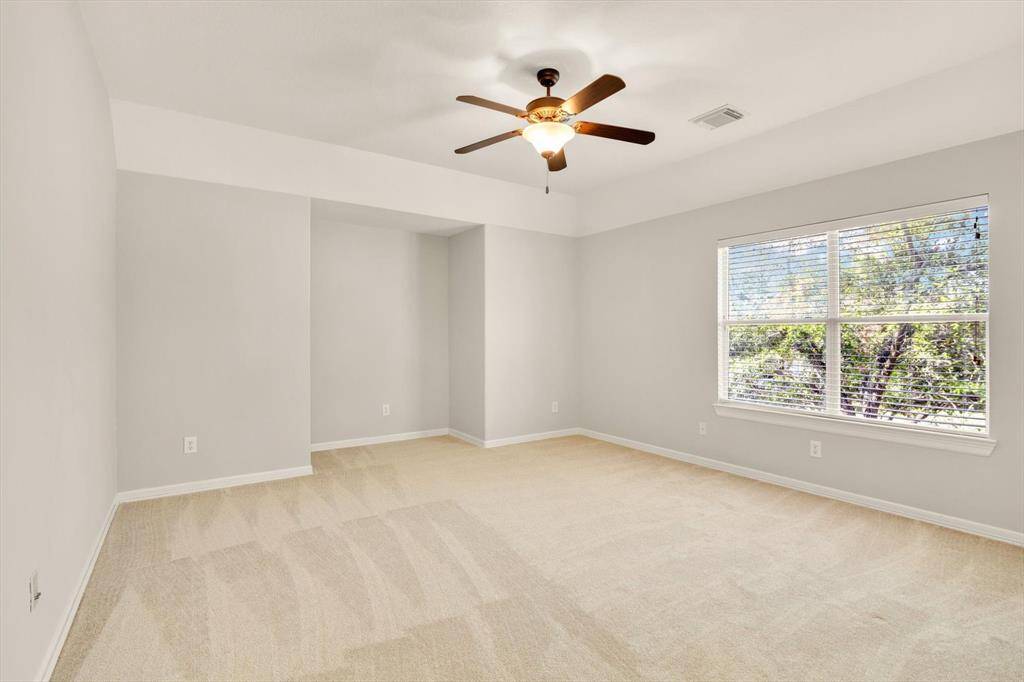Game room features soft beige carpeting, light gray walls, and ample natural light from a large window. A ceiling fan adds comfort and style to the room.