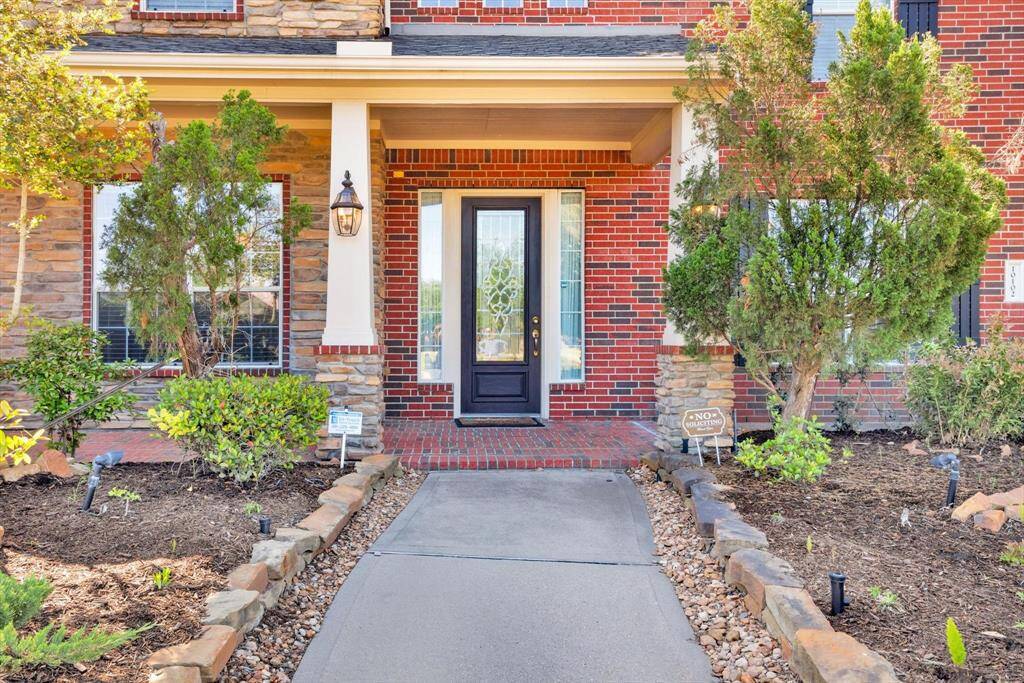 Charming brick and stone exterior with a welcoming front porch. The entryway features a stylish black door flanked by sidelights, surrounded by manicured landscaping and a stone-lined walkway. Ideal for creating a warm first impression.