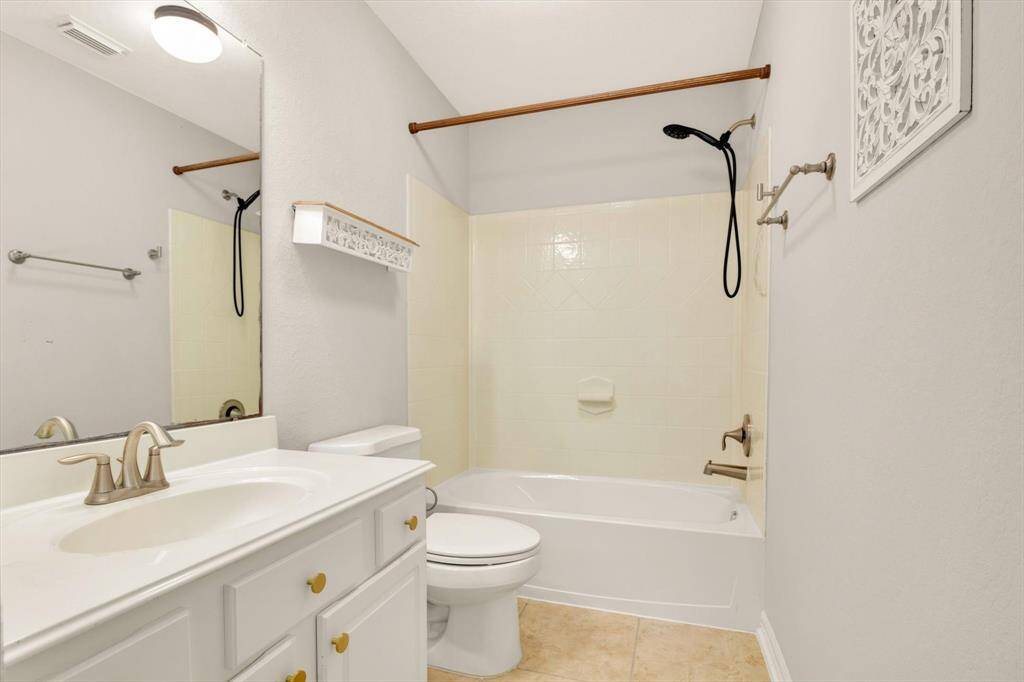 Secondary bathroom features a clean, modern design with light walls and tile flooring. It includes a bathtub with a shower, a white vanity with storage, and a large mirror, creating a bright and functional space.