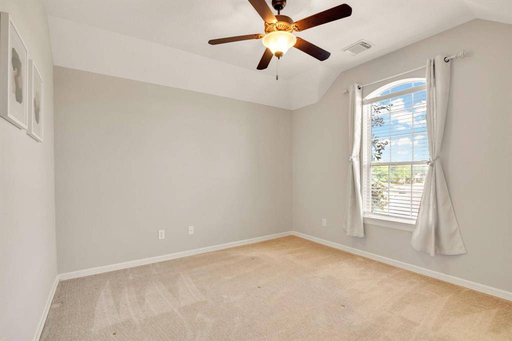 Secondary Bedroom features neutral walls and carpet, a ceiling fan with light, and a large window with drapes, providing plenty of natural light. Perfect for a bedroom or office space.
