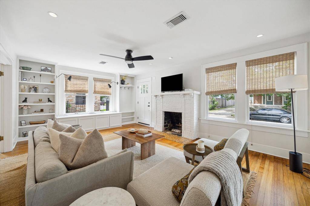 Another view of the inviting living room that features a cozy white brick fireplace, built-in shelves, and large windows with bamboo shades.