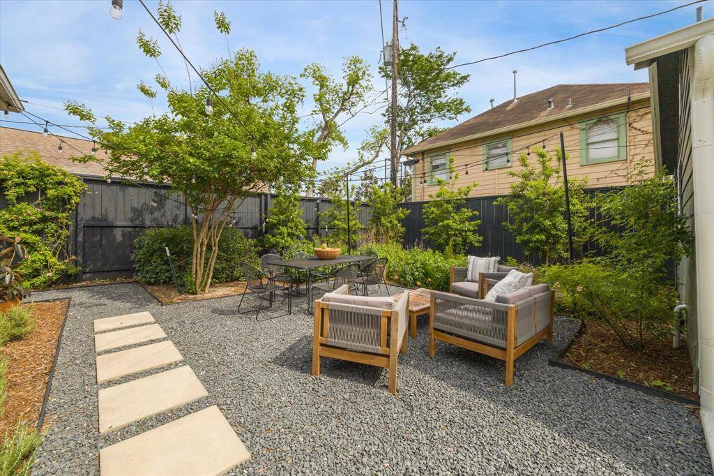 Charming backyard featuring a gravel patio with string lights, modern outdoor furniture, and lush landscaping, creating an inviting space for relaxation and entertaining.