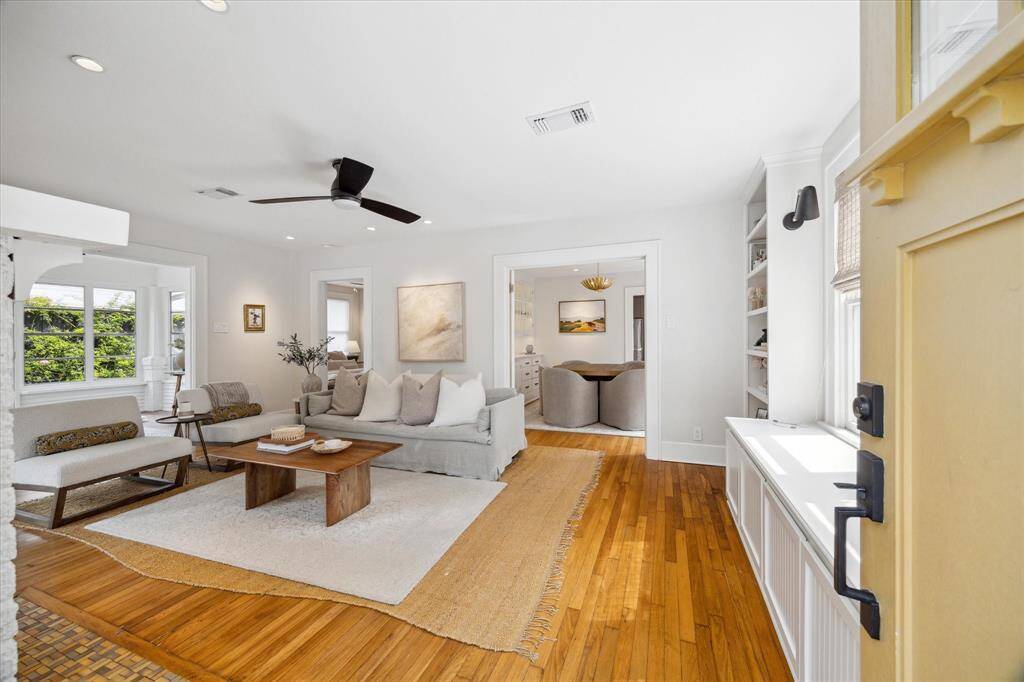 Bright and inviting living room with hardwood floors, a modern ceiling fan, and a cozy seating area. The space is open to the dining area, featuring built-in shelves and ample natural light, creating a welcoming atmosphere.
