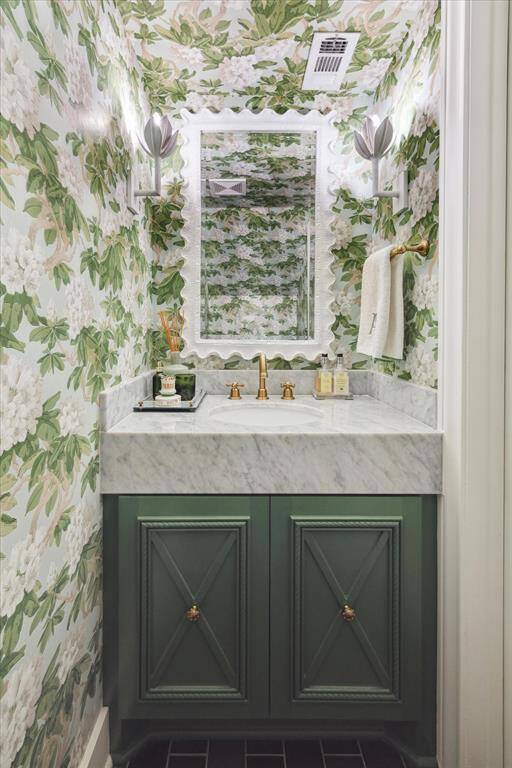 This charming powder room, located on the first floor, is decorated with an OKA Mirror that compliments the floral design of the Cole and Son Wallpaper, Visual Comfort sconces, unlacquered brass door knob on a custom cabinet and a gorgeous Carrera marble countertop.