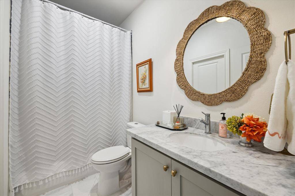 The en-suite bath features a pristine shower-tub combination, a spacious and beautiful Carrera marble vanity. The room is beautifully enhanced with Pottery Barn brass hardware, a brass sconce and a decorative rattan mirror.