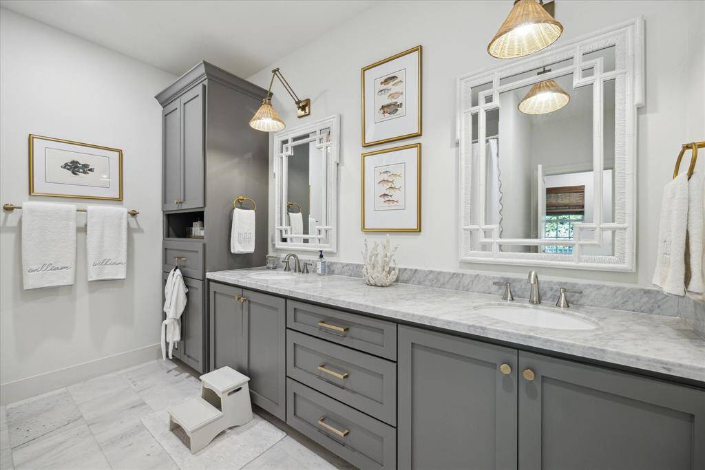 This full bath, adorned with Carrera marble and contemporary accents, is both stunning and practical due to its dual sink vanity. It is located near two of the upstairs bedrooms.