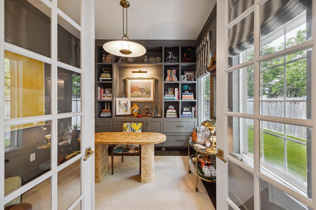 Well-designed French doors lead into this beautiful study that offers custom window treatments and extensive built-in cabinetry that contribute to the overall elegant aesthetics and functionality of the room.