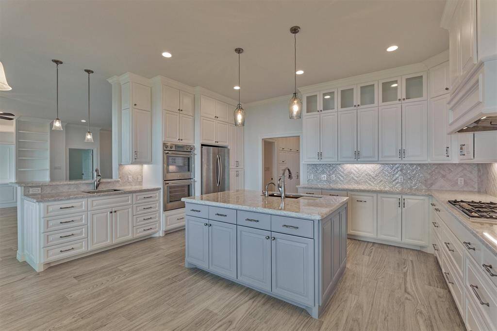 The kitchen island showcases a soft blue finish that pairs beautifully with the Cambria quartz countertops, creating a cohesive and stylish focal point. Designed with functionality in mind, the island offers storage on both sides for added convenience. The prep sink at the peninsula is complemented by custom wine cabinets, with the option to install a wine refrigerator, if desired.