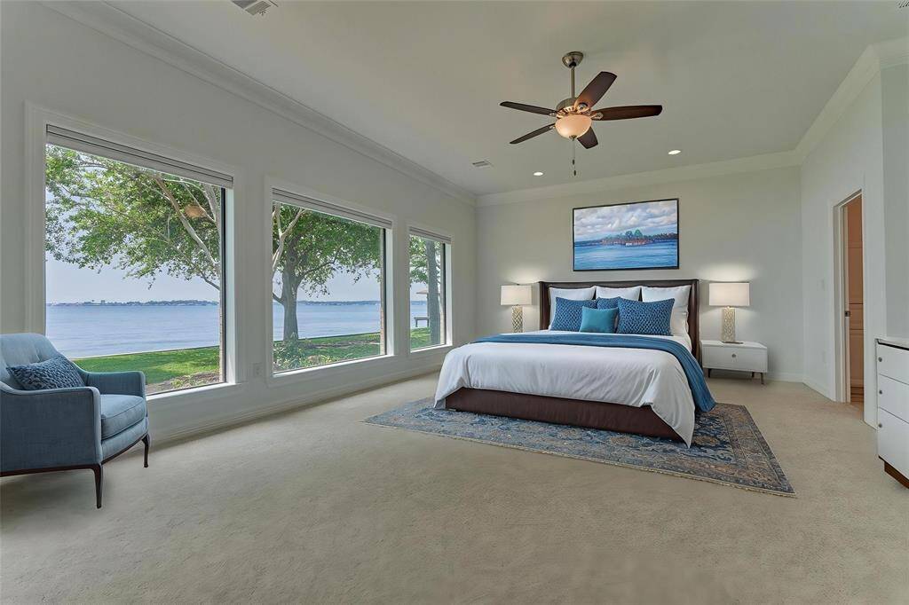 The first primary bedroom features three expansive windows offering a panoramic view of the lake. New carpet, double crown molding and neutral finishes create a custom and calming space. Photo has been virtually staged to show furniture placement. All carpet in the home is Shaw brand, comfort quiet nylon.
