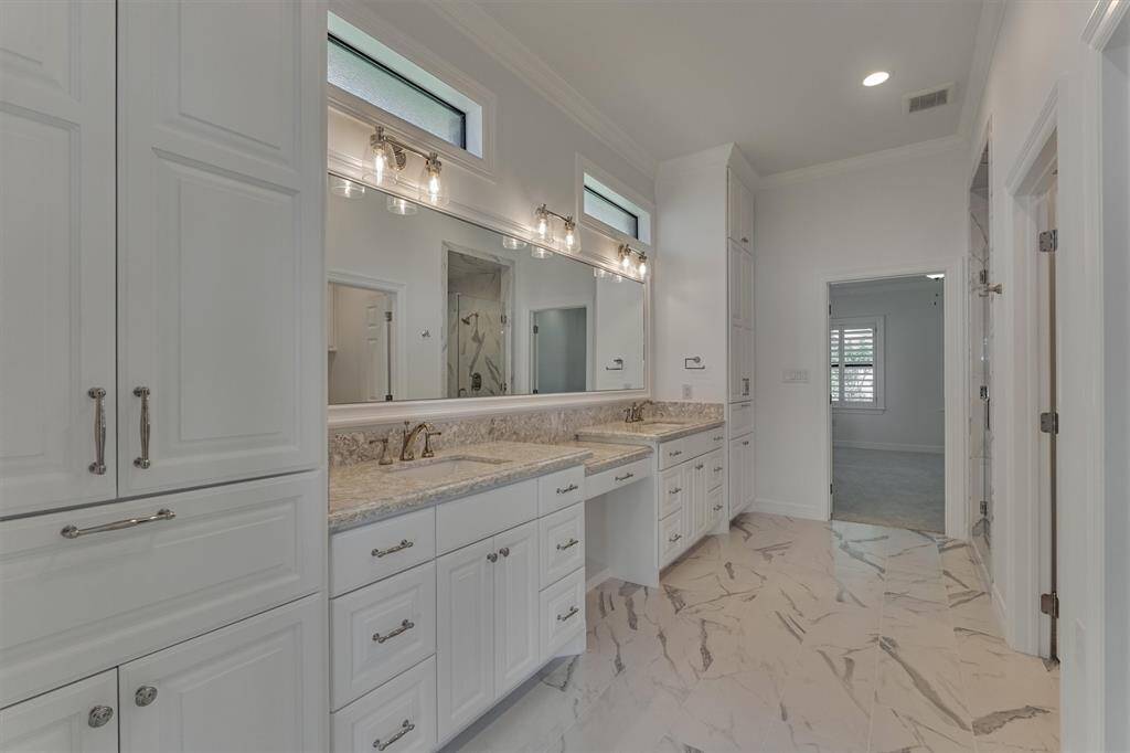 The primary bath serves as a stylish and functional connection between the two primary bedrooms. It features double sinks, a dedicated vanity area, and custom cabinetry—all topped with elegant Cambria quartz countertops. Floor-to-ceiling cabinets provide ample storage and include a built-in laundry hamper that can be easily converted to shelving, offering flexibility to suit your needs.