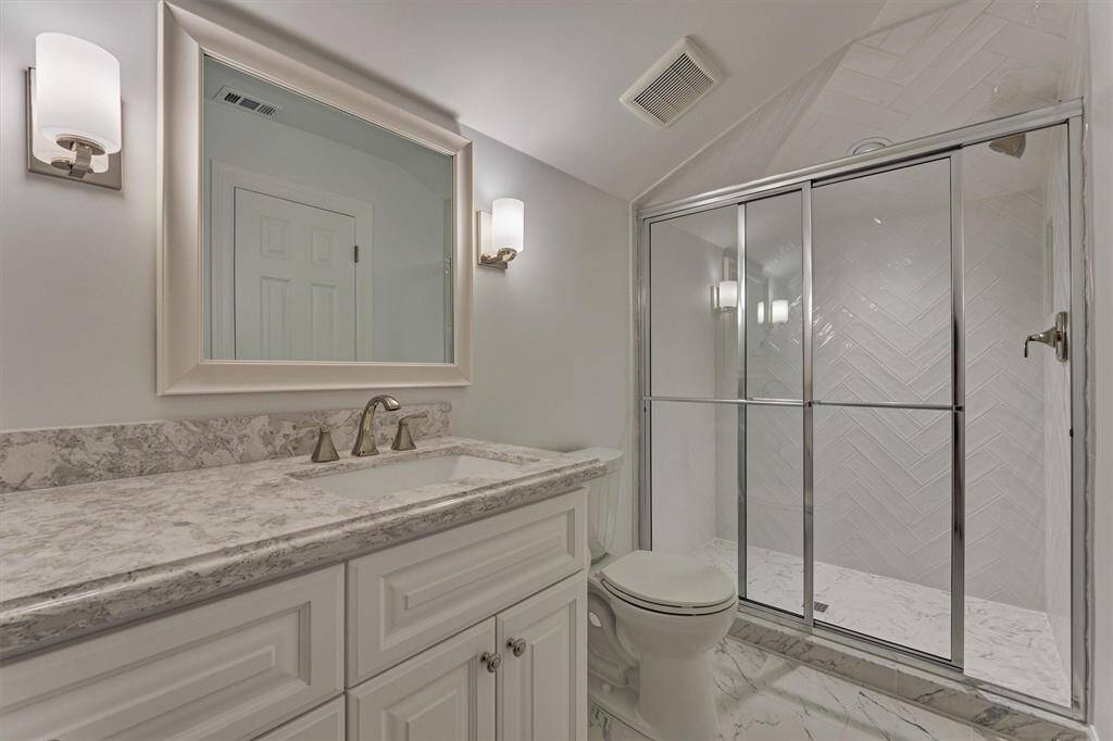 The full bath on the second floor showcases a walk-in shower with an elegant herringbone tile pattern, a sleek vanity topped with a quartz countertop, and romantic lighting that adds a warm, inviting ambiance.