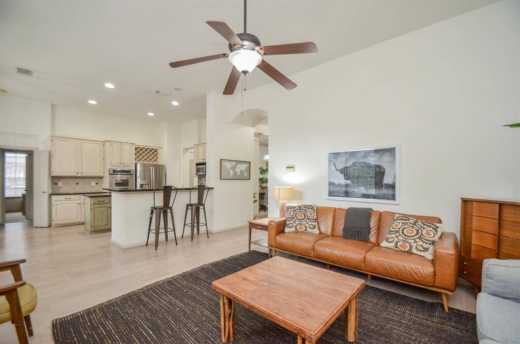 This is a spacious, open-concept living room with a modern kitchen, featuring stainless steel appliances, painted cabinetry, and a breakfast bar. The living area is well-lit and complemented by a neutral color palette.