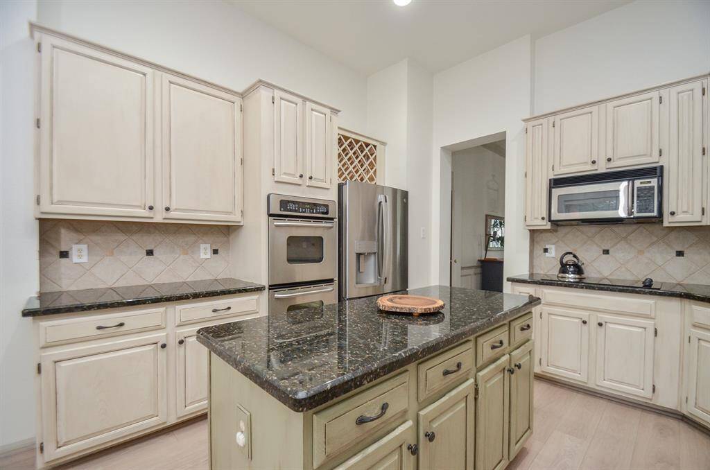 The kitchen features cream-colored cabinetry with ample storage, dark granite countertops, and modern stainless steel appliances. A central island provides additional workspace and storage.