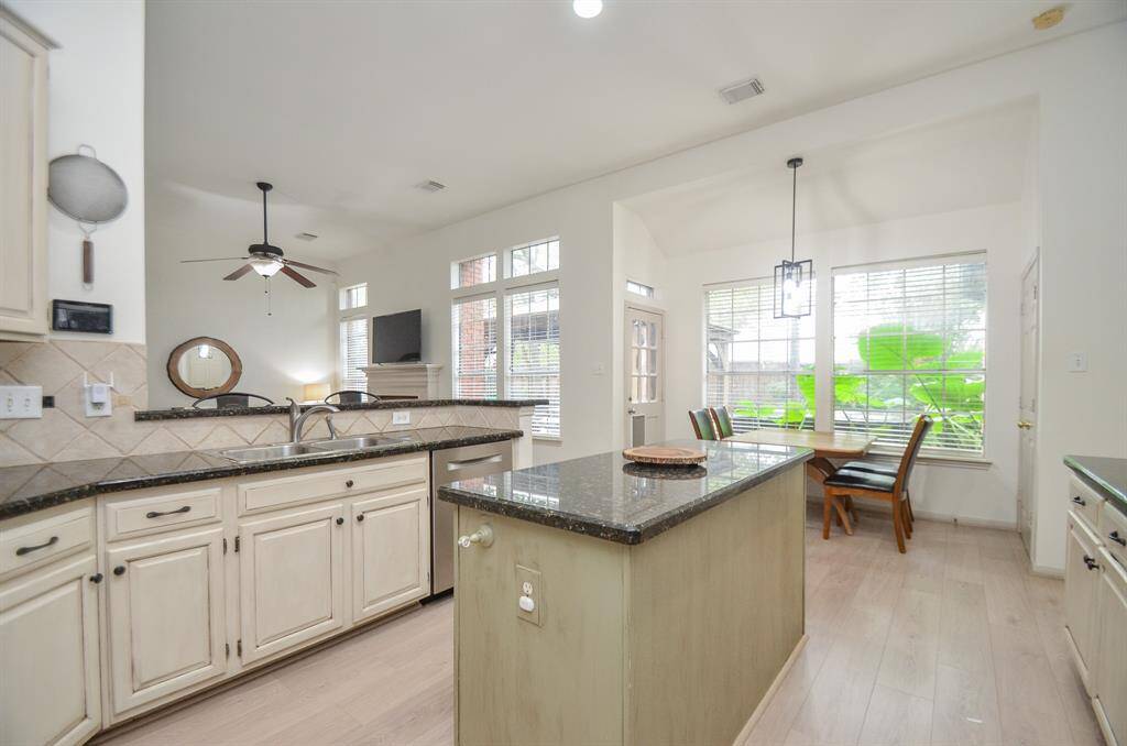This is a bright, modern kitchen with painted cabinetry, granite countertops, stainless steel appliances, and a breakfast nook by large windows that provide plenty of natural light. The space features easy to care for luxury vinyl flooring
