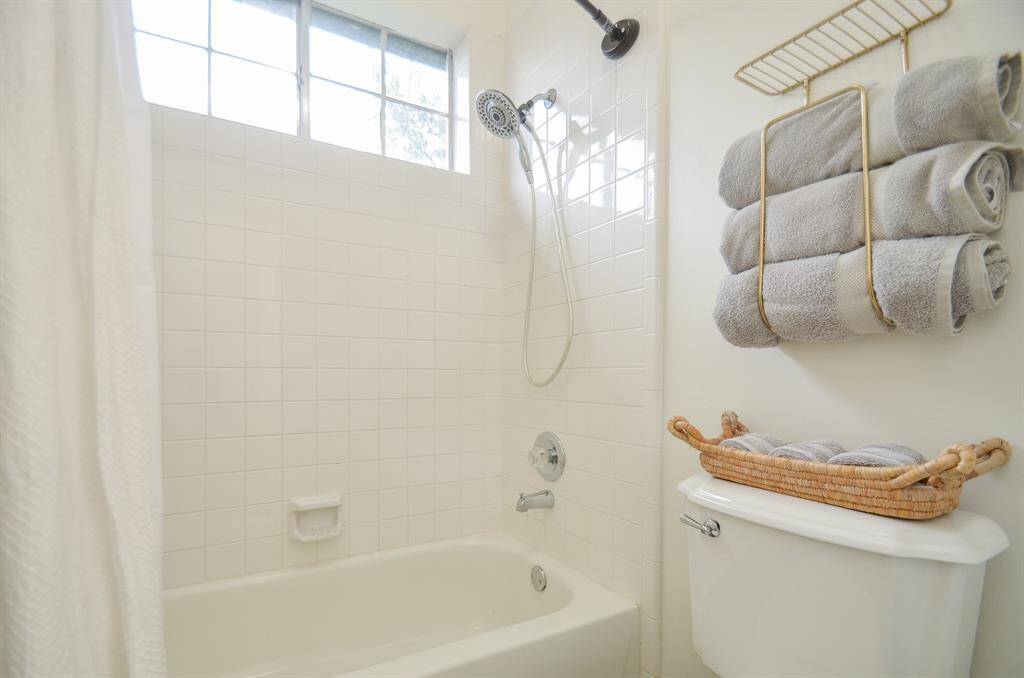 This is a clean and bright bathroom featuring a white bathtub with an overhead shower, tiled walls, and a window for natural light.