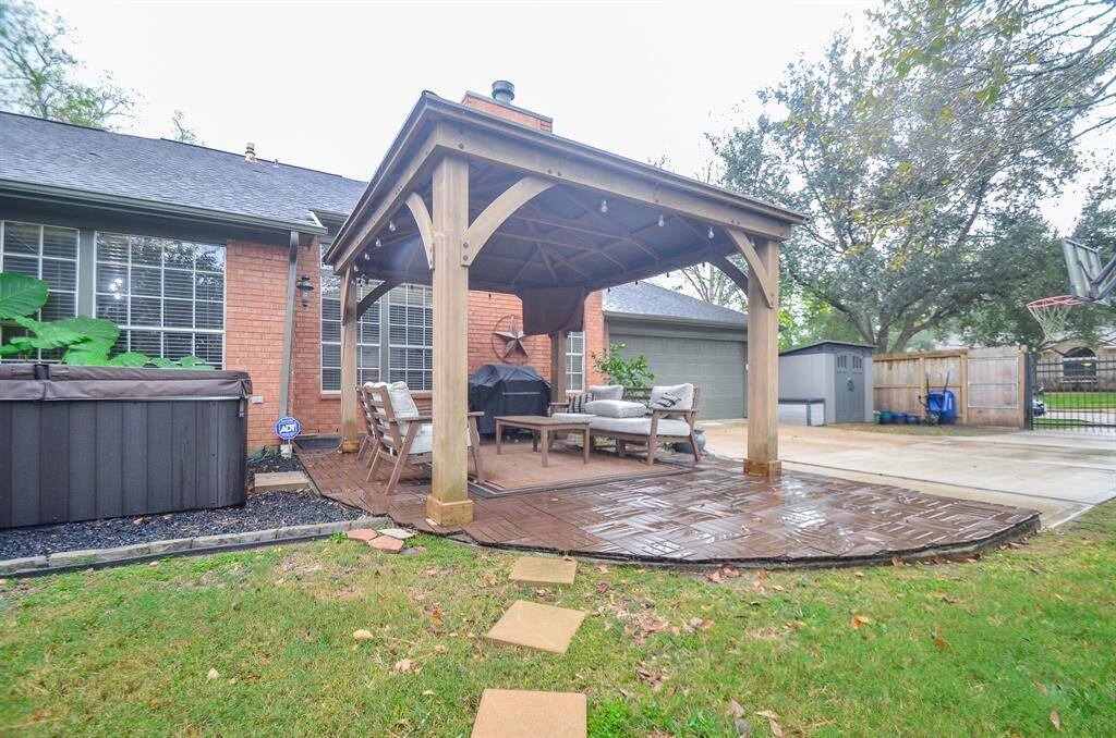 This backyard features a spacious covered patio with a comfortable seating area, an inviting hot tub, and a well-maintained lawn, perfect for relaxation and entertainment.