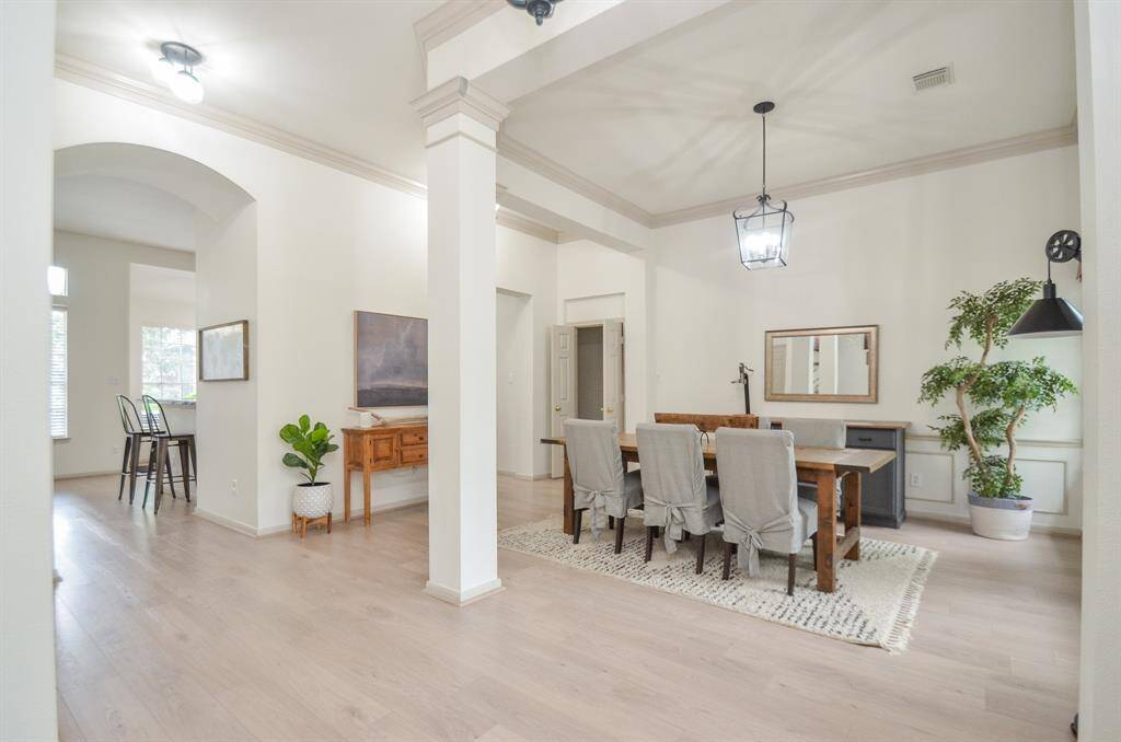 This is a spacious and well-lit dining area featuring elegant flooring, high ceilings with crown molding, and sophisticated lighting fixtures. The room is complemented by neutral wall colors, giving it a modern and inviting atmosphere.