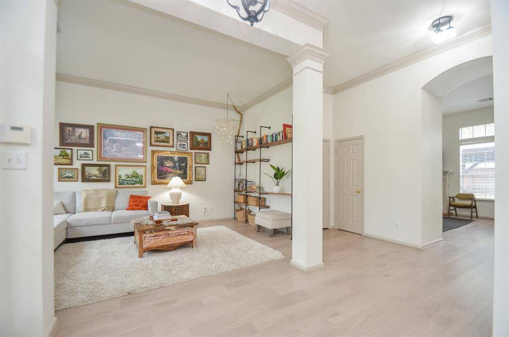This is a spacious, well-lit living room with high ceilings, elegant archways, and modern flooring. The room is complemented by a neutral color palette.