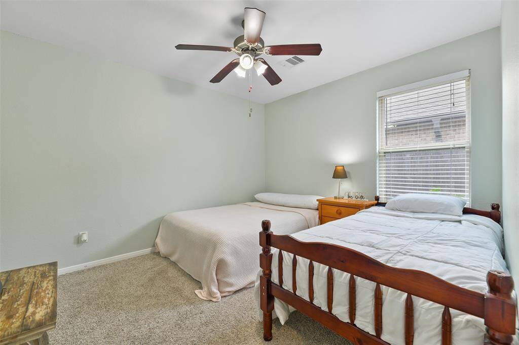 The first of two secondary bedrooms features a lighted ceiling fan, a soft sage paint on the walls, plush carpet, a side-facing window dressed with 2-inch blinds, and a generous walk-in closet.