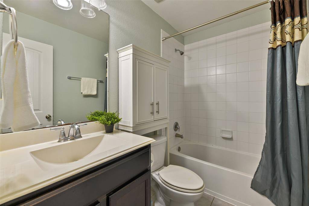 In the guest bathroom, find a cultured marble countertop with a rectangular basin sink, polished chrome faucet, espresso-stained cabinetry, tile floors, and a combination bathtub and shower with a classic white tile surround.