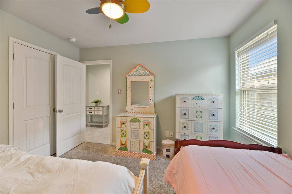 The third and final bedroom in the home features a colorful lighted ceiling fan, a soft sage green paint selection, plush carpet, an ample closet, and a side-facing window dressed with 2-inch blinds.
