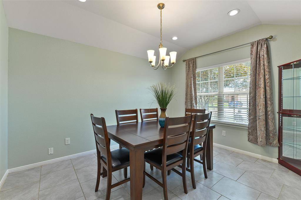 To the right of the foyer, an inviting dining room beckons guests with an elevated gambrel ceiling, a 5-light chandelier, and an expansive front-facing window dressed with 2-inch blinds.