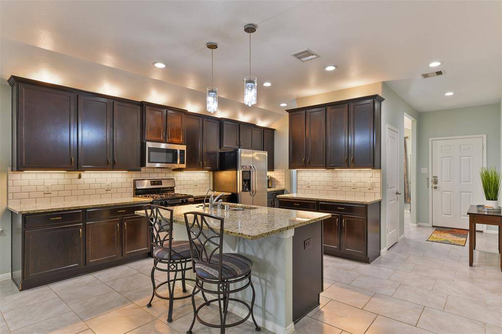 Just beyond the dining room, you'll find this lovely island kitchen with fine finishes that include espresso-stained wood cabinetry with under & over cabinet lighting, granite countertops, a subway tile backsplash, and island seating topped by a pair of pendant lights.