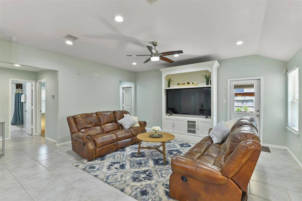 Looking into the family room, note the open and airy feel with light-colored tile floors, a soft sage paint, ample lighting, and a split floorplan with the guest bath and secondary bedrooms off to the left and the master suite at the far end, just beyond the family room.
