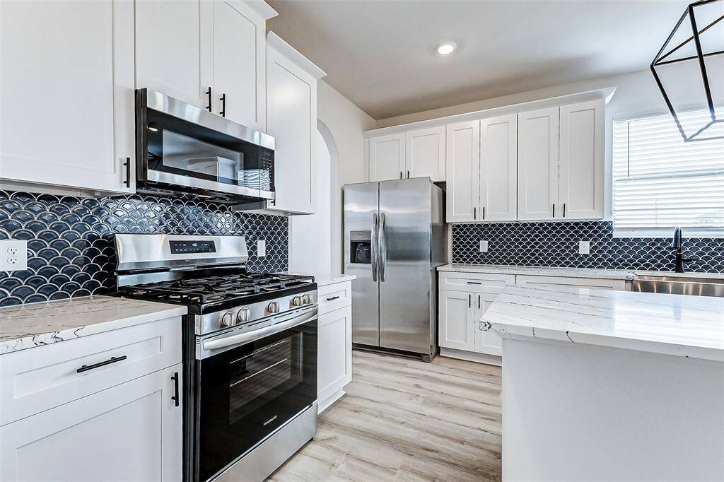 A closer look at the gourmet cooking space highlights the stainless steel gas range and built-in microwave, framed by crisp white cabinetry and a deep navy backsplash. This kitchen is designed for both aesthetic appeal and practicality, offering plenty of counter space for meal prep and entertaining. **This is a picture of a Rylan Floor Plan from another Saratoga Homes.**